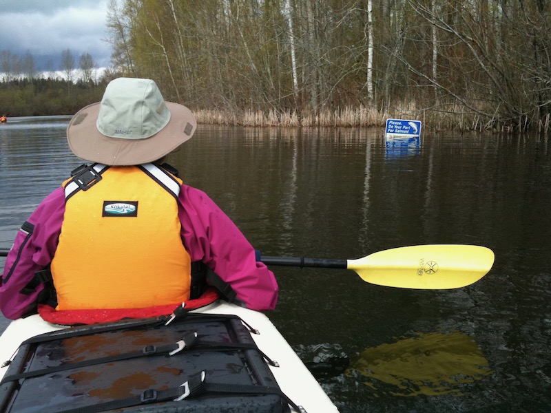 Melanie in front of kayak looking at partially submerged sign