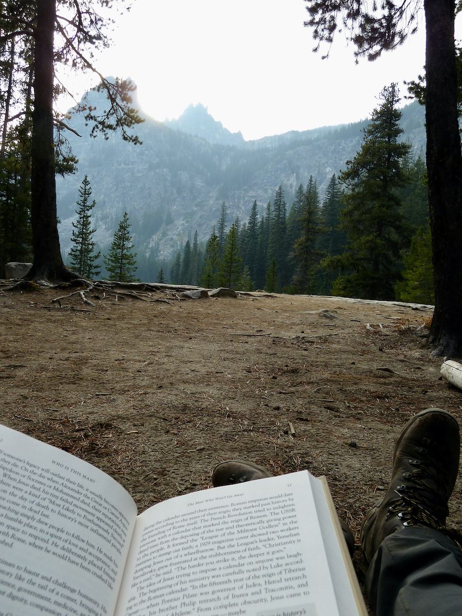 book in lap with peaks in distance