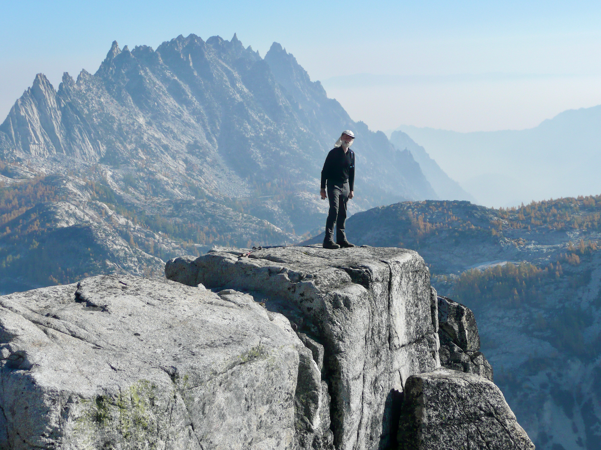 Larry standing on a square rocky point with mountain peaks in distance