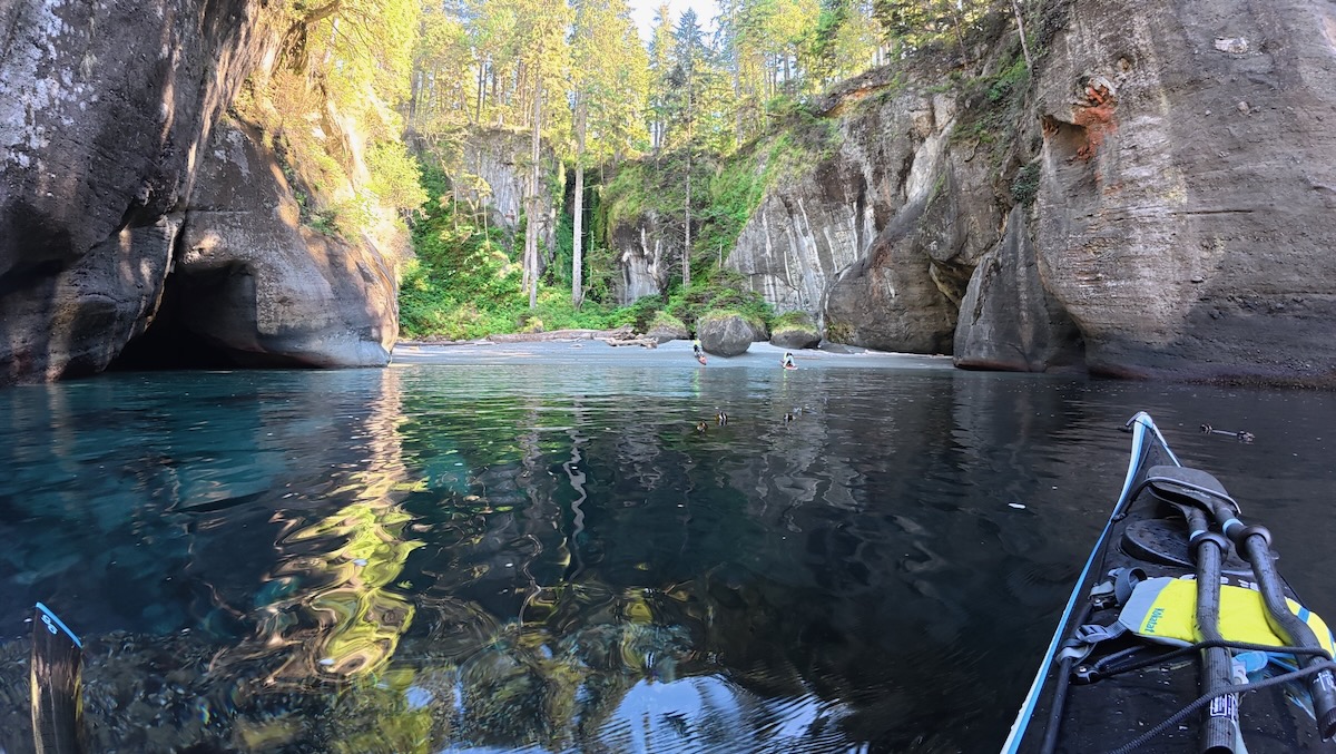 small beach with trees at back, rock on both sides with caves