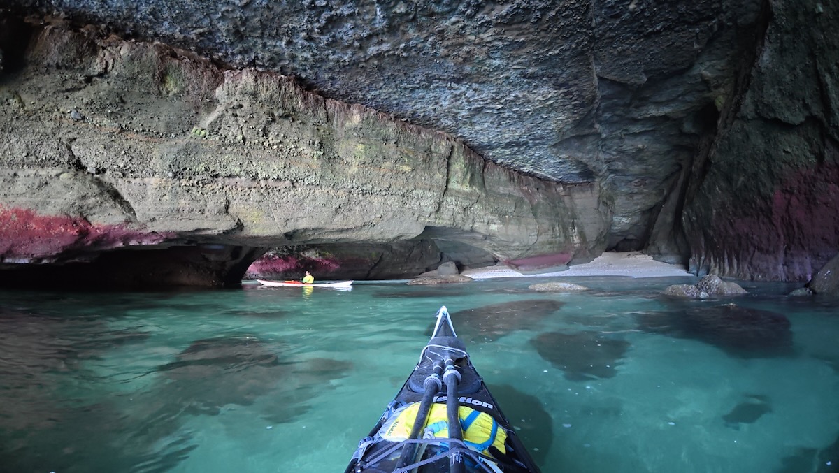 large cave with colored rocks and clear sea water