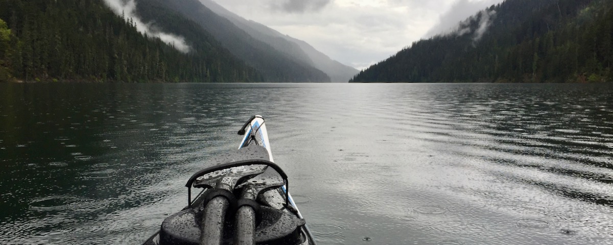 Lake with rain-drops, kayak bow, gray skies and hills